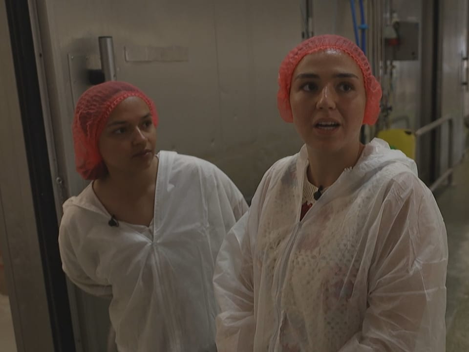 Zwei Frauen in Schutzkleidung und roten Haarnetzen in einer Fabrik.
