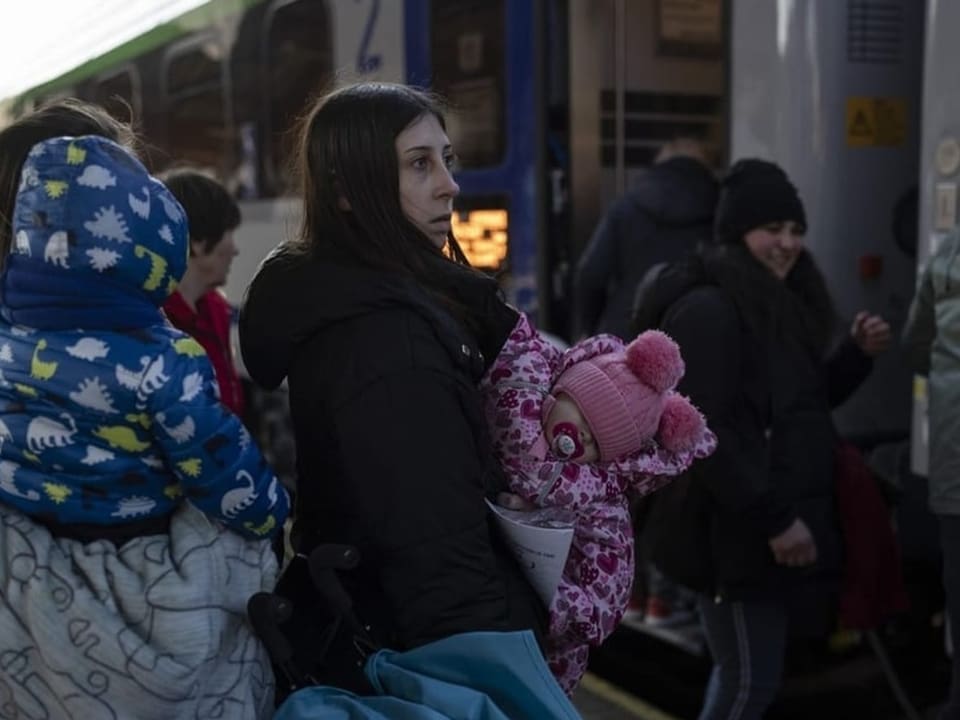 Frau mit zwei Kindern vor einem Zug.