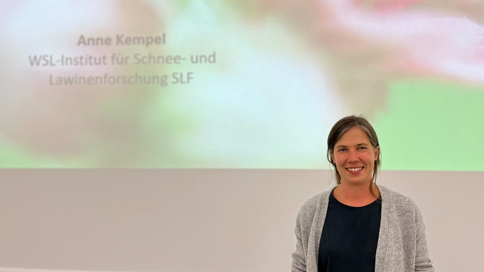 Anne Kempel vor einer Projektionsleinwand mit dem Text 'Anne Kempel WSL-Institut für Schnee- und Lawinenforschung SLF'.