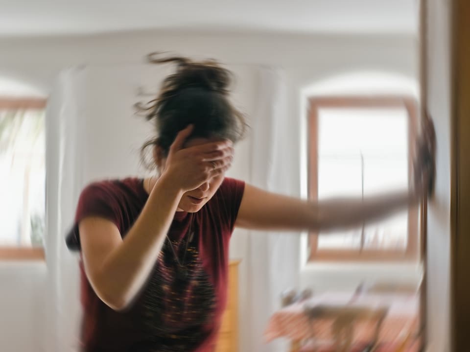 A woman has a headache and leans on the door frame while holding a hand to her forehead.