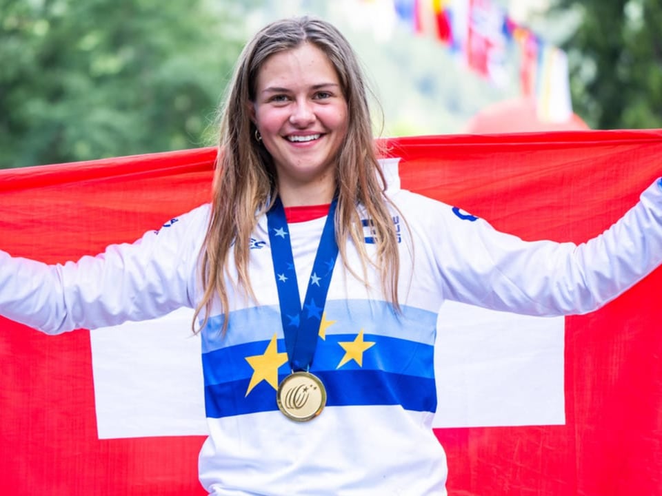 Frau hält Schweizer Flagge und trägt Medaille.