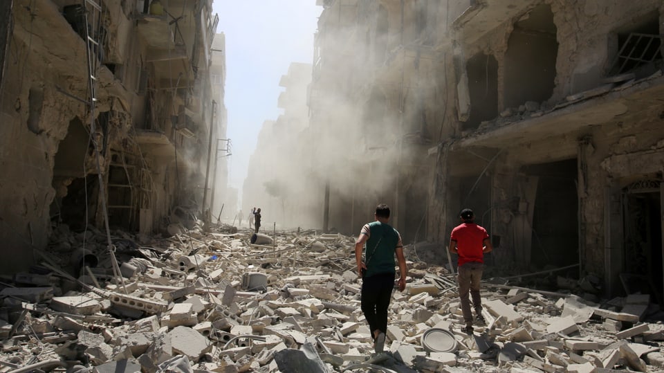 Häuserschlucht in Aleppo mit der Trümmerübersähten Strasse dazwischen und zwei Menschen darin