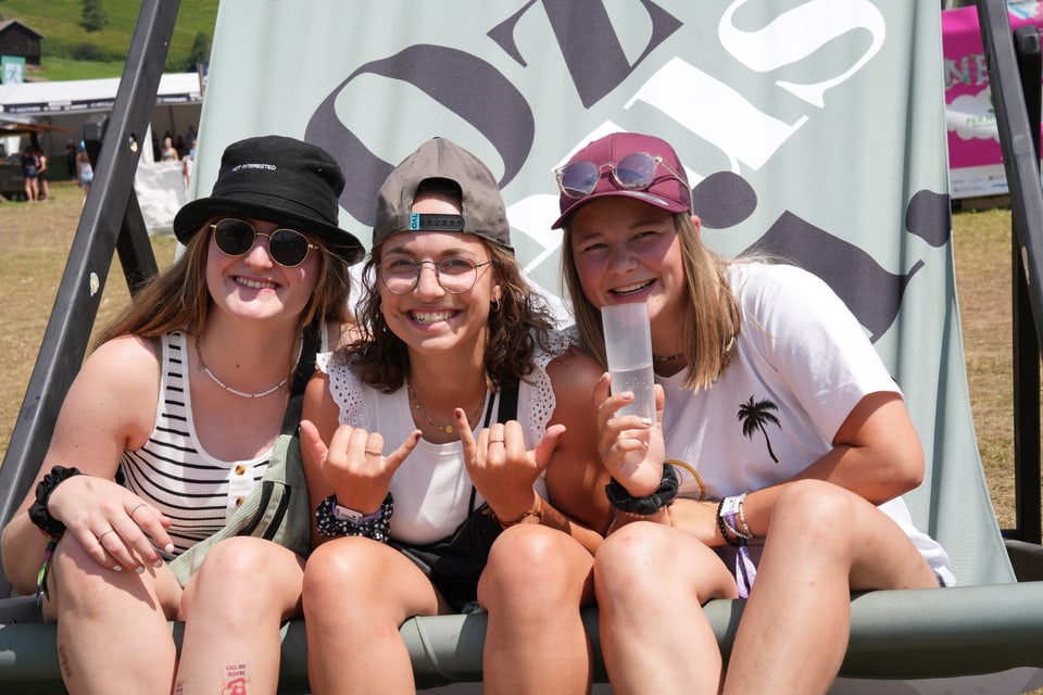 Drei lachende Frauen auf einem grossen Stuhl bei einem Festival am Open Air Lumnezia 2024.