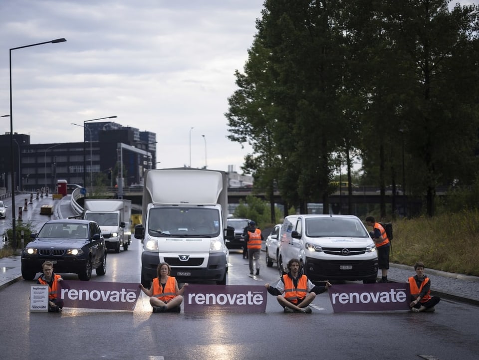 Klimaaktivistinnen und -aktivisten sitzen mit Bannern auf der Strasse.