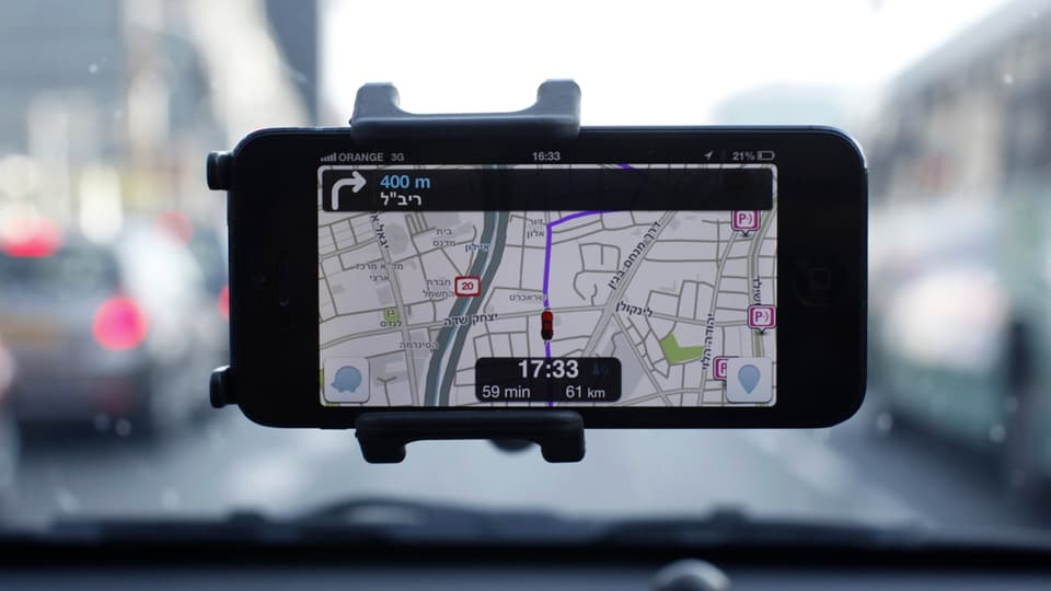 Ein Handy klebt an einer Windschutzscheibe, installiert die Verkehrs-App Waze.