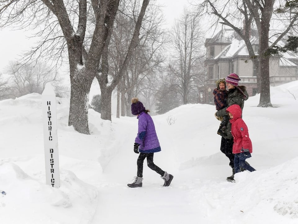 Frau mit Kind am Arm und zwei Kinder nebenbei läuft durch den Schnee. Rundherum ist alles weiss. 