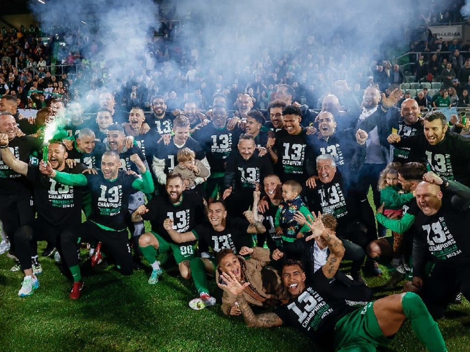 Fussballmannschaft feiert Sieg mit grünen Rauchfackeln auf dem Spielfeld.