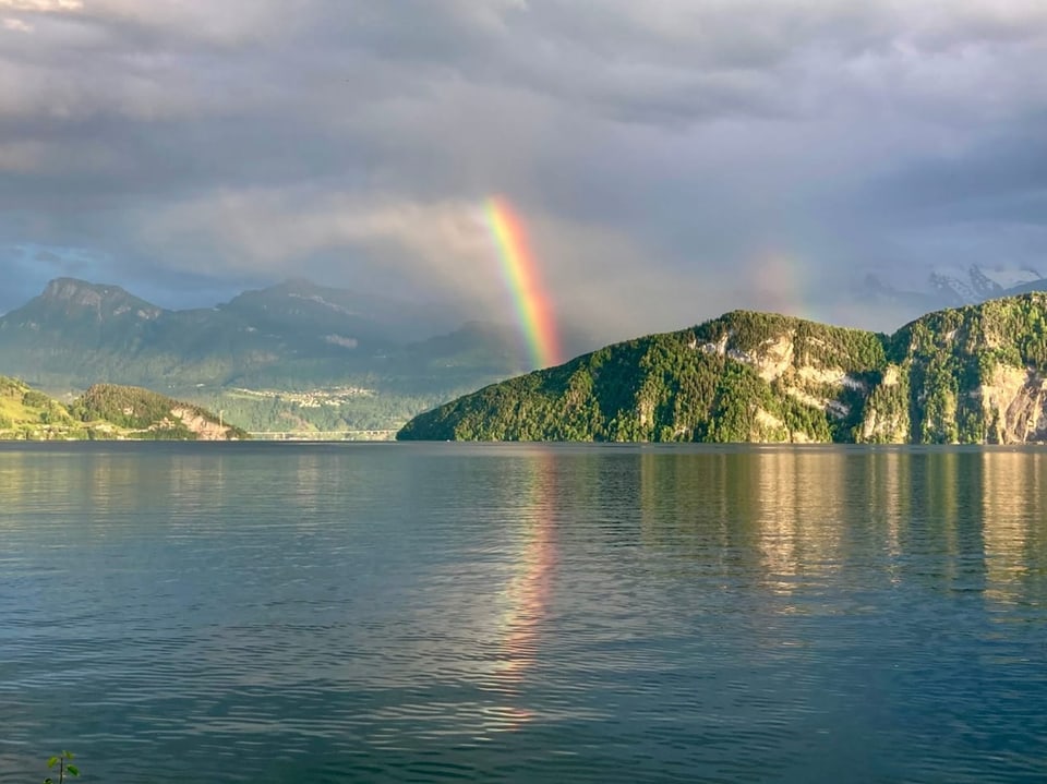 Regenbogen über einem See mit Bergen im Hintergrund.