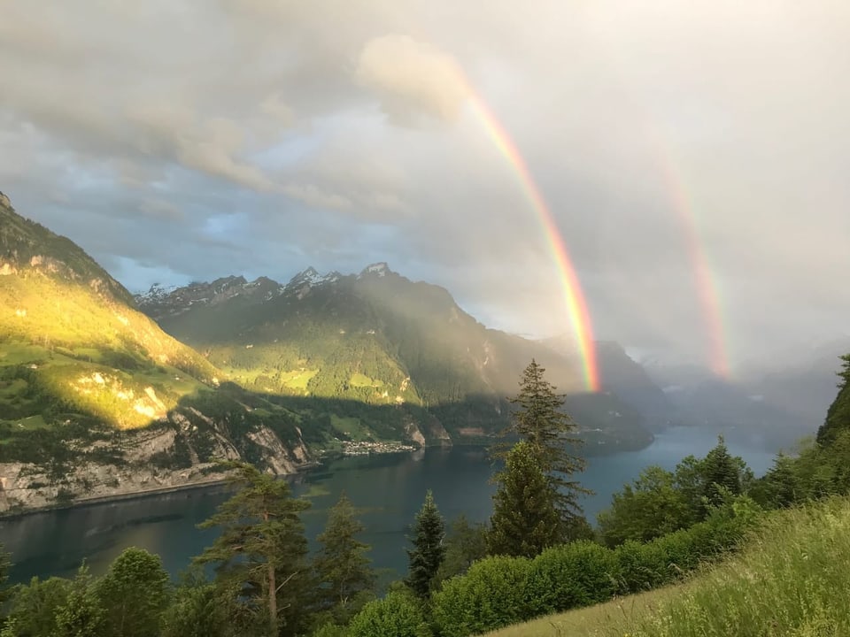 Doppelter Regenbogen über einem Berg- und Seetal.