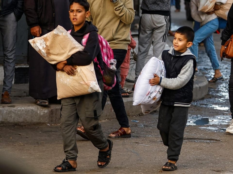 Vertriebene palästinensische Kinder tragen Habseligkeiten auf ihrem Weg nach Hause.