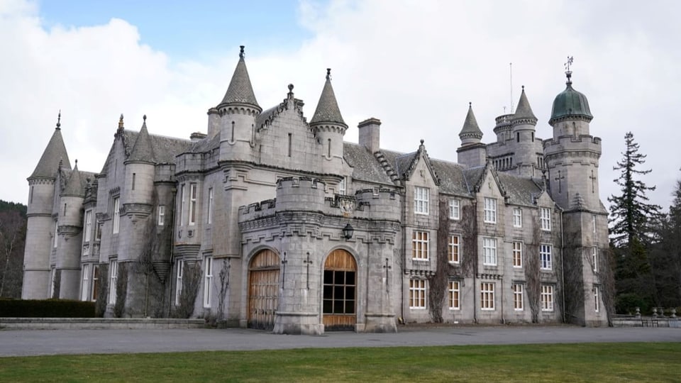 Balmoral Castle in Scotland is a gray stone building with numerous small towers and a large wooden gate. 