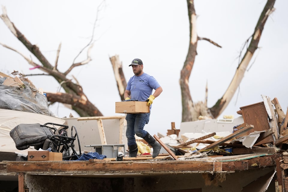 A man carries a box through the rubble after the tornado.