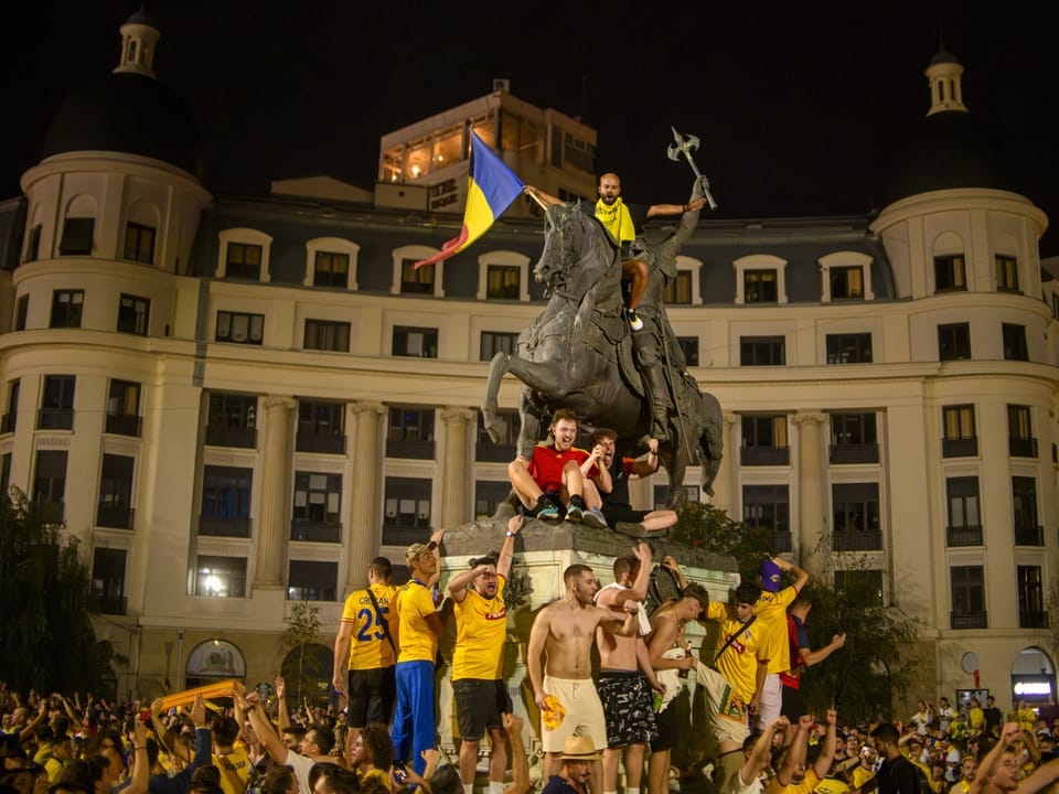 Fussballfans feiern an einer Pferdestatue in Bukarest ausgelassen.