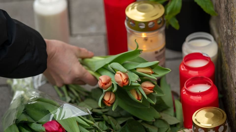 Eine Person legt Tulpen neben Kerzen beim Tatort der beiden getöteten Polizisten.