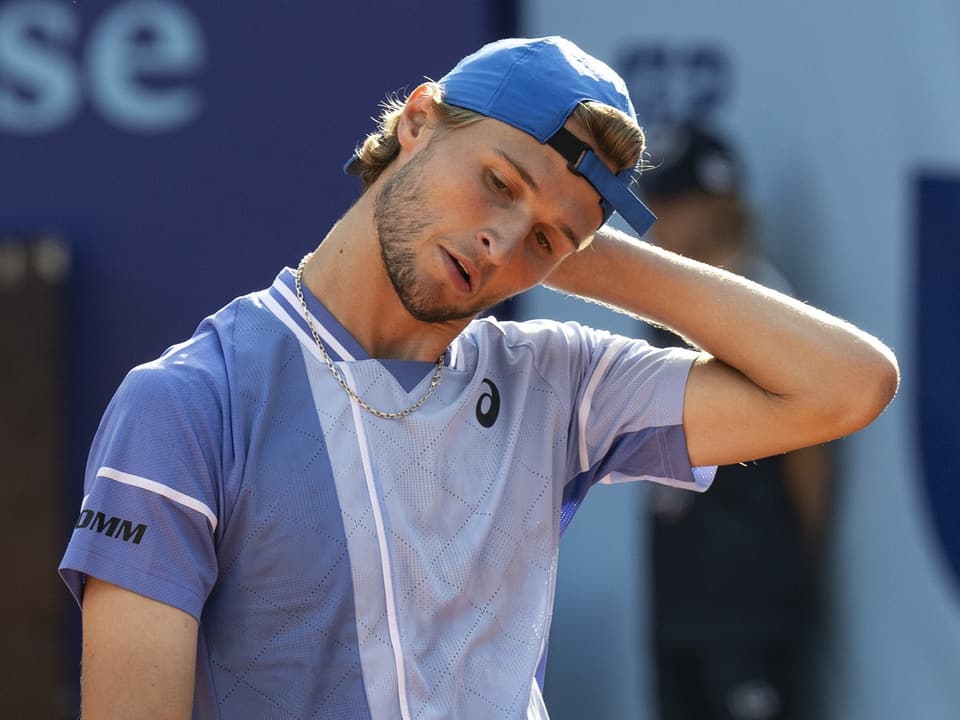 Tennisspieler in lila Shirt und blauer Kappe kratzt sich am Nacken.