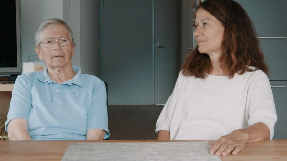 Ältere Frau und mittelalte Frau sitzen an einem Tisch in einem Raum.