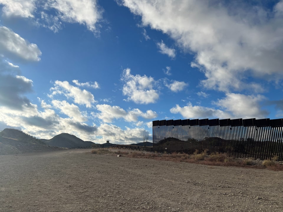 Wüstenlandschaft mit einem Zaun und bewölktem Himmel.