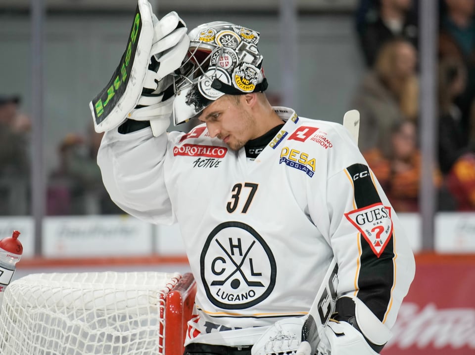 Eishockeytorwart in weissem Trikot hebt den Helm.