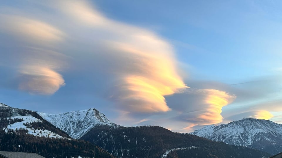 Schneebedeckte Berge mit leuchtenden, lenticularen Wolken am Himmel.