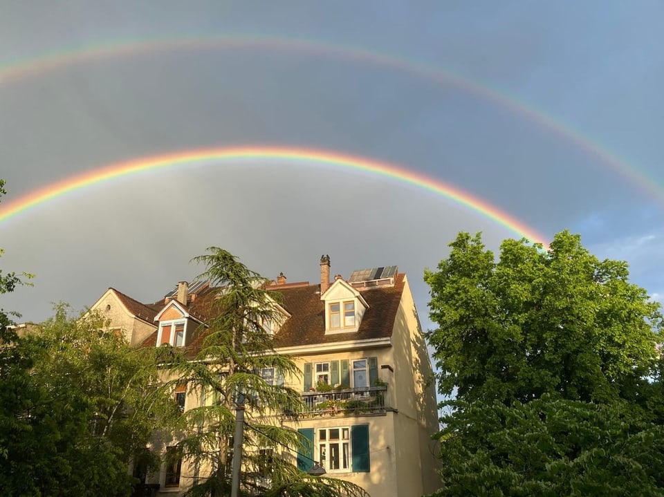 Doppelter Regenbogen über einem Haus mit Bäumen.