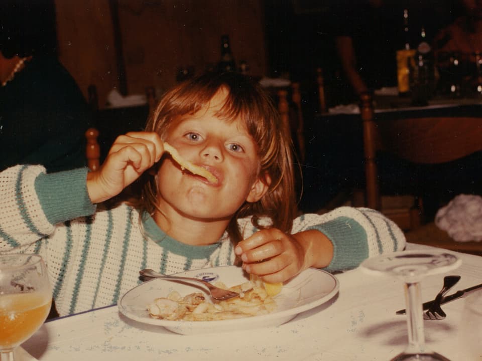 Ein kleines Mädchen sitzt beim Essen am Tisch eines Restaurants.