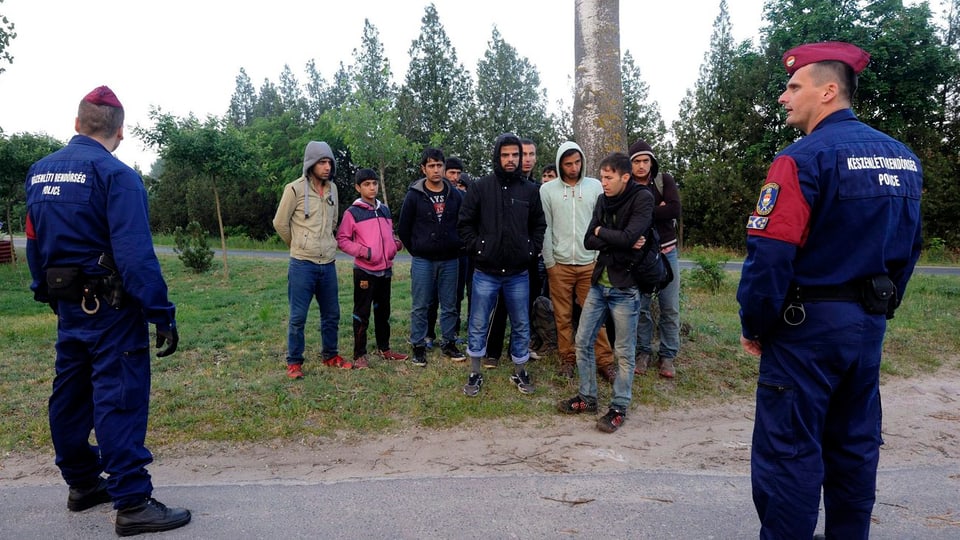 Zwei ungarische Grenzwächter stehen vor einer Gruppe von illegalen Einwanderern.