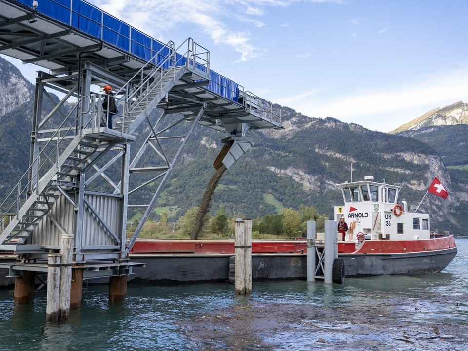 Boot neben Förderband an Bergsee mit Kies.