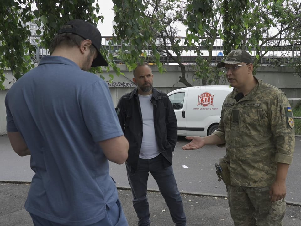Drei Männer stehen draussen und sprechen miteinander, einer in Militäruniform.