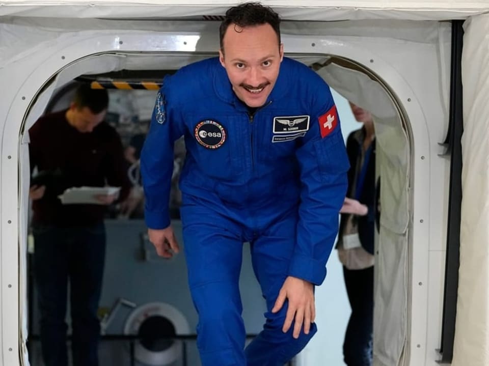 Astronaut in blauem Raumanzug steigt aus einer Luke.