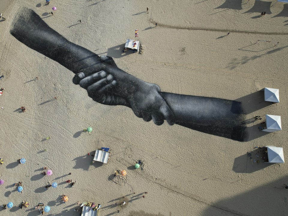 Ein Fresko auf Sand. Es zeigt zwei Arme, die ineinander verschlungen sind.