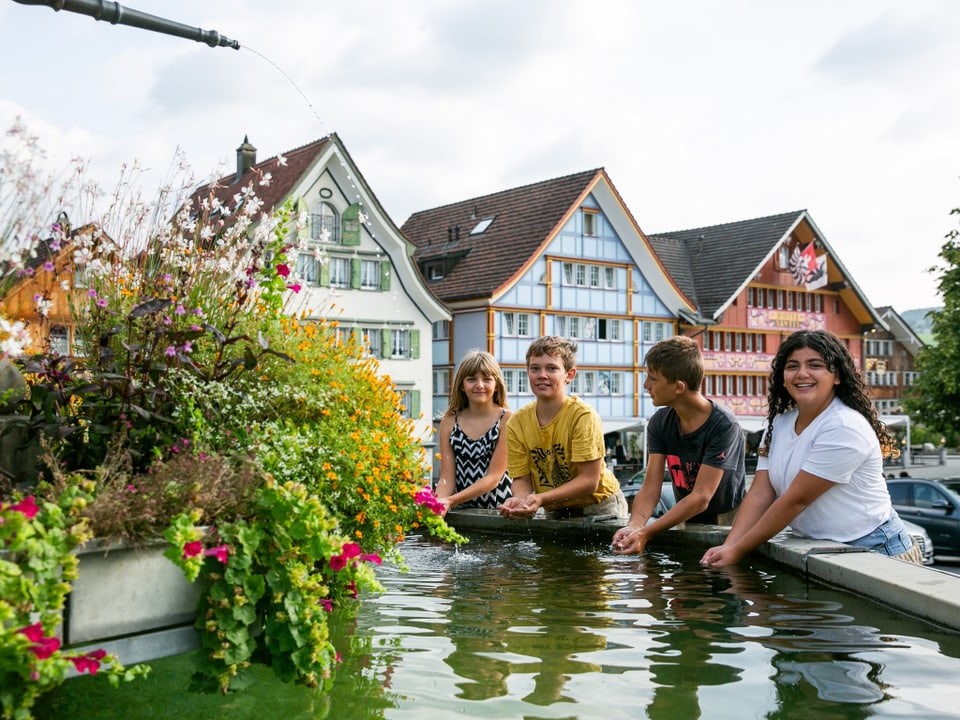 Kinder stehen an einem Brunnen und sammeln Wasser mit den Händen.