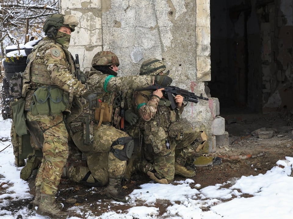 Drei Soldaten in Tarnkleidung knien vor einer Ruine im Schnee.