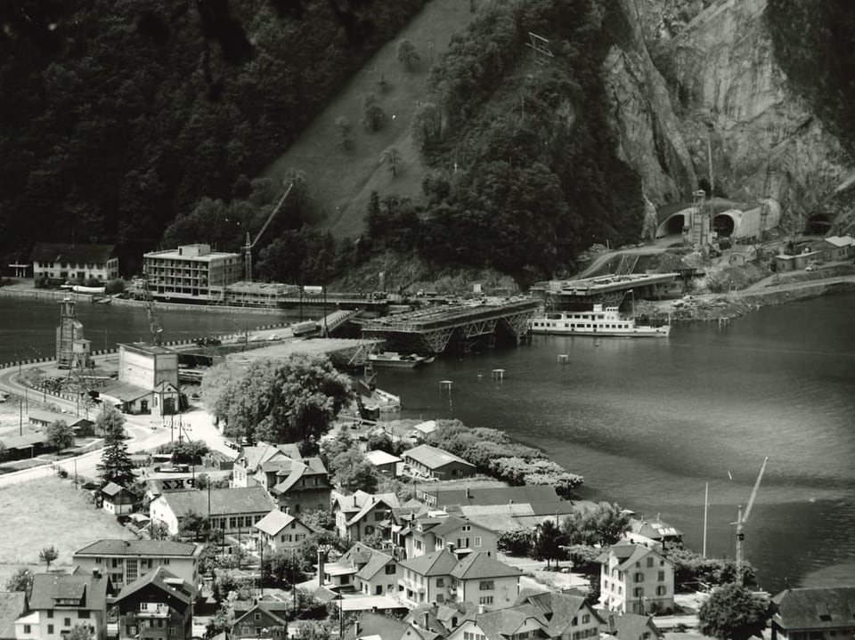 Historische Stadt am See mit Bergen und Tunneln im Hintergrund.