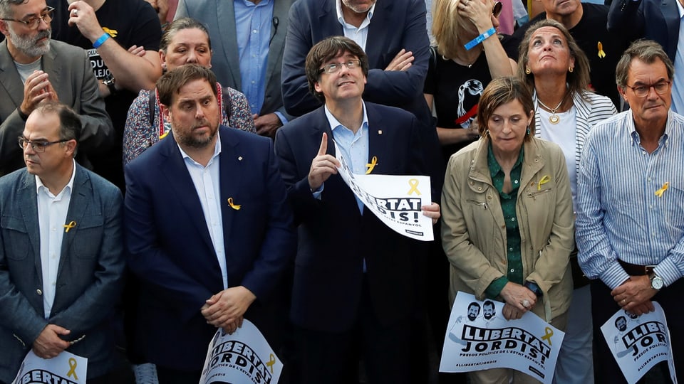Männer und Frauen stehen in einer Menge, Puigdemont mit Brille blickt nach oben.