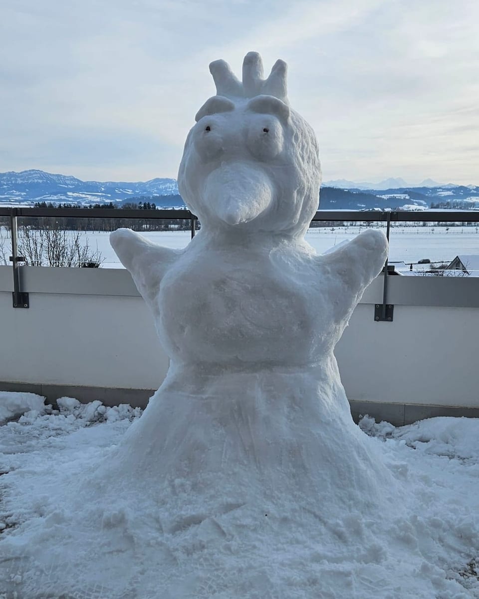 Schneeskulptur einer Figur mit grossen Augen und einem Schnabel auf Terrasse.