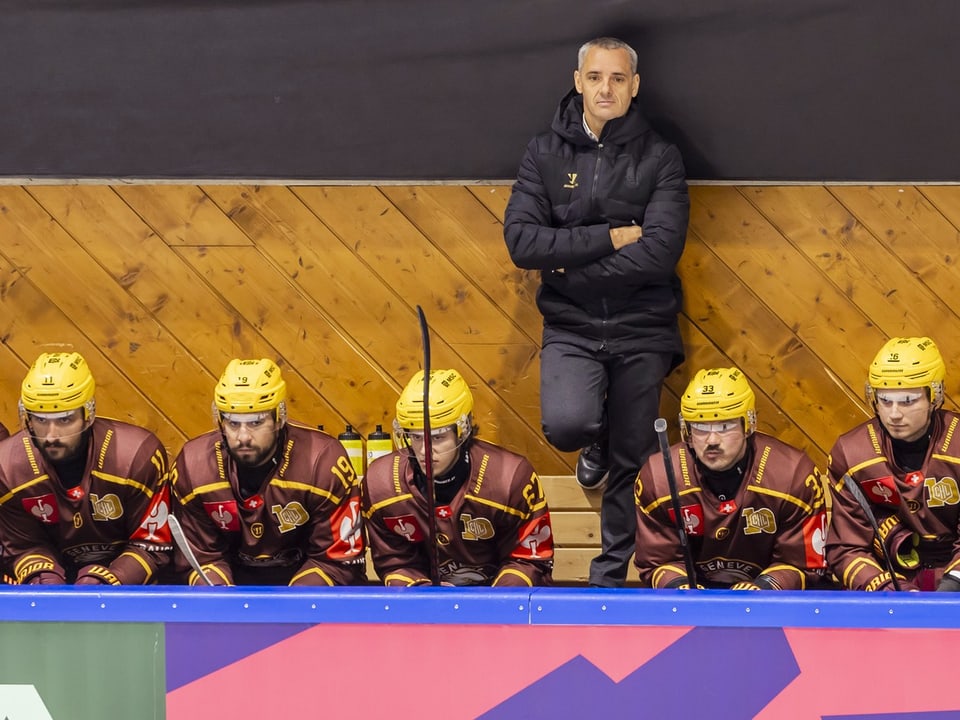 Eishockeyspieler auf der Bank mit Trainer im Hintergrund.