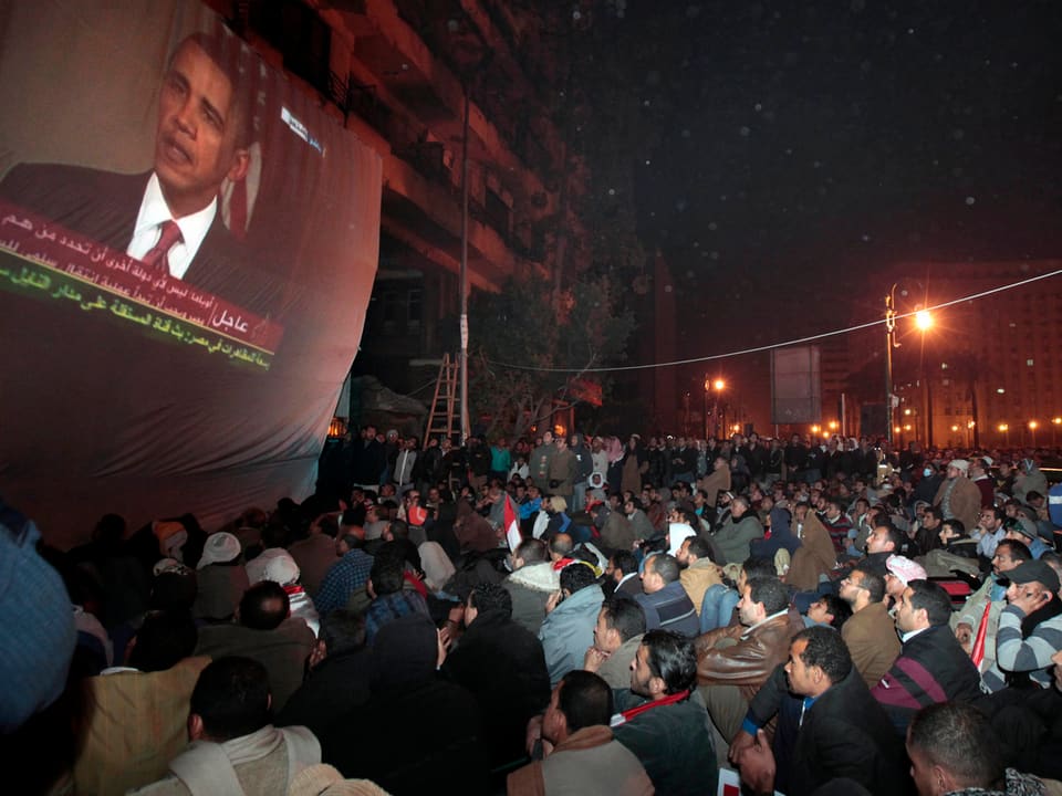 Obama auf einem Bildschirm, Menschen sehen auf einem Platz zu.