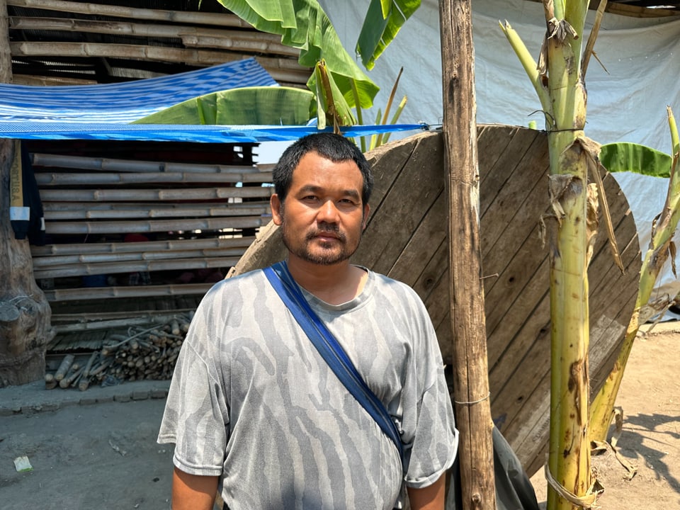 Mann steht vor ländlicher Hütte unter Bananenstauden