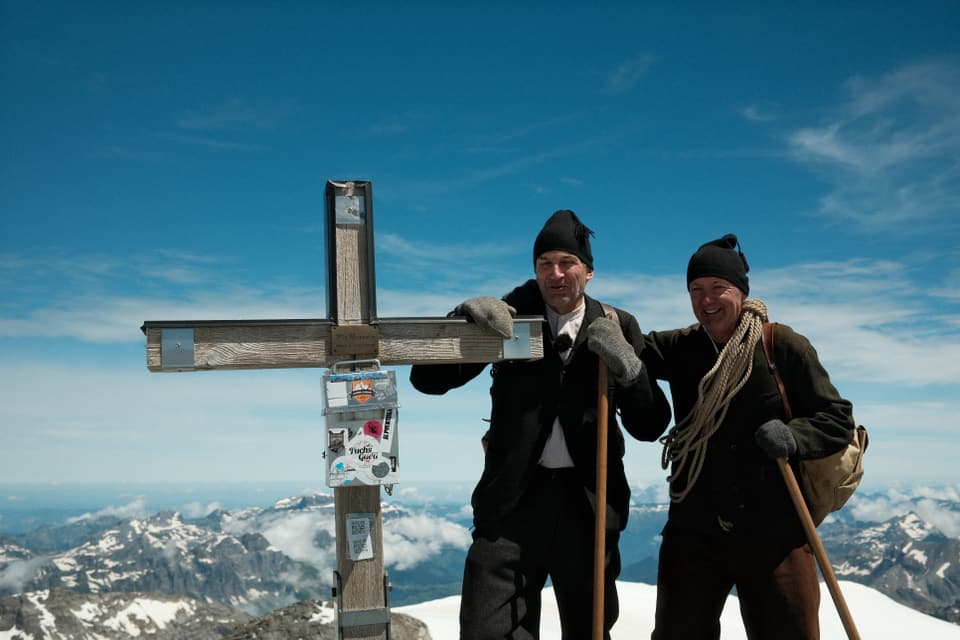 Zwei Bergsteiger posieren an einem Gipfelkreuz.