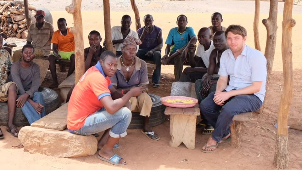 Reporter Fabian Urech sitzt auf einem Dorfplatz in Ghana.