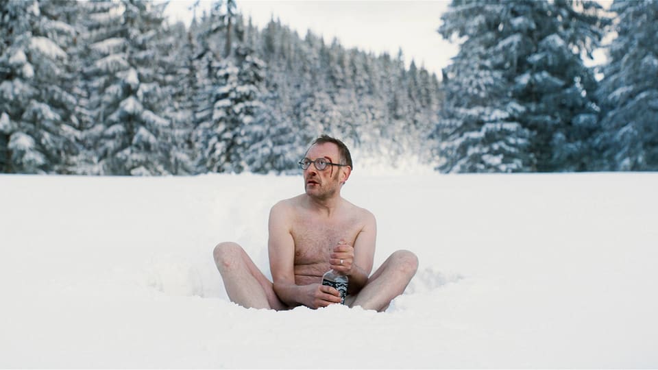 Ein nackter Mann sitzt im Schnee.