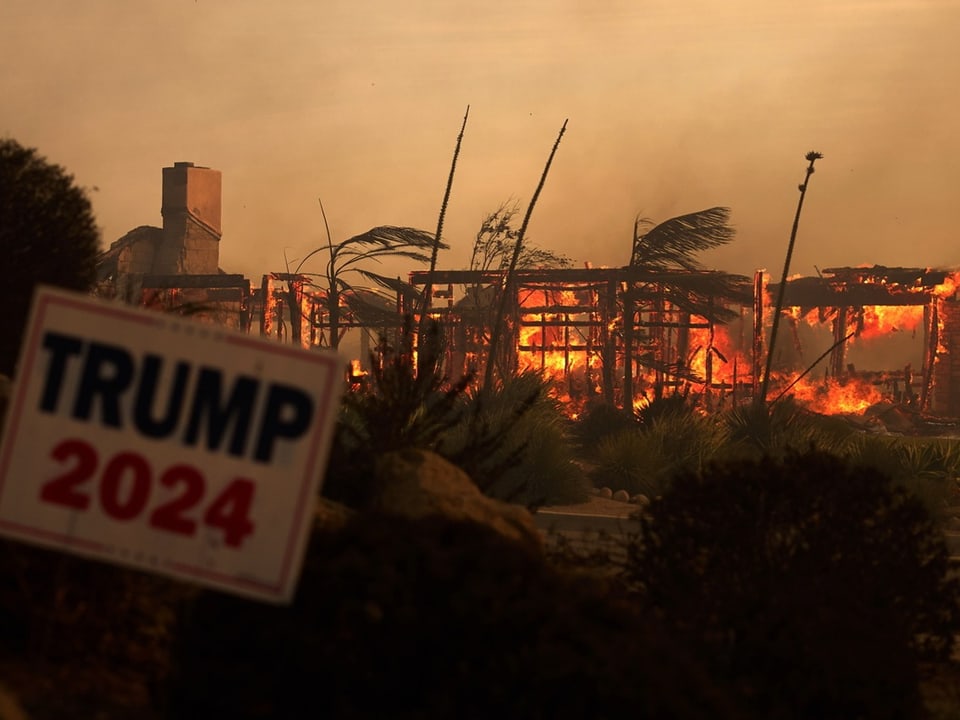 Brennendes Gebäude mit Trump 2024 Schild im Vordergrund.