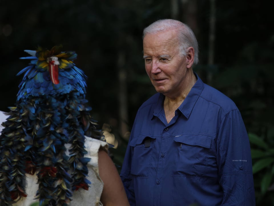 Mann im blauen Hemd mit person in buntem Kopfschmuck im Wald.