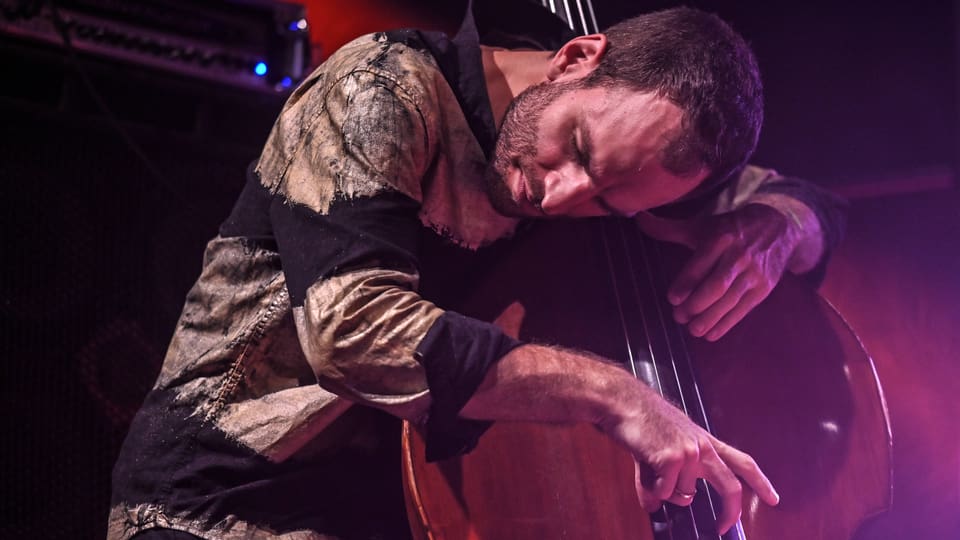 Mann mit braunen Haaren und Bart beugt sich über sein Instrument (Bass) und hat seine Augen geschlossen