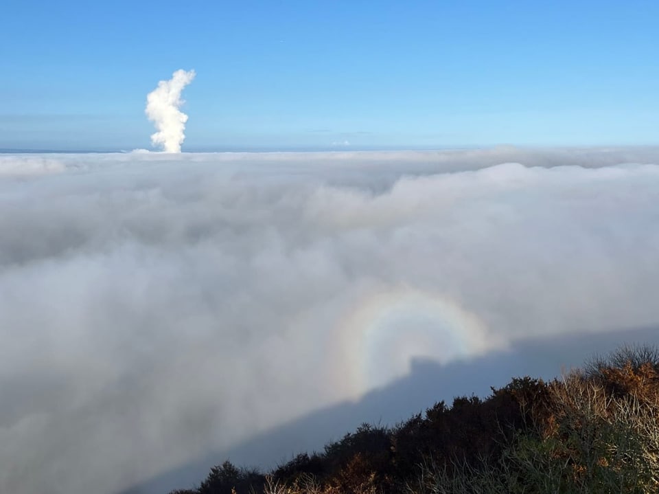 Blick auf eine Nebellandschaft mit einem farbigen Lichtring und Wolken am Himmel.