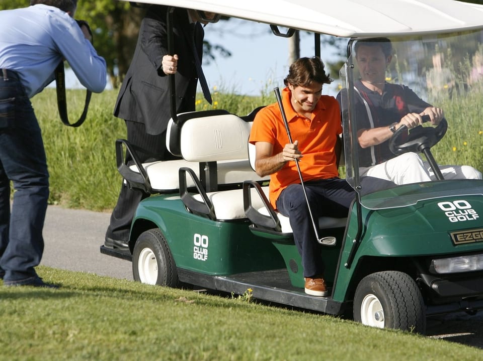 Männer fahren in einem Golfwagen über einen Golfplatz.