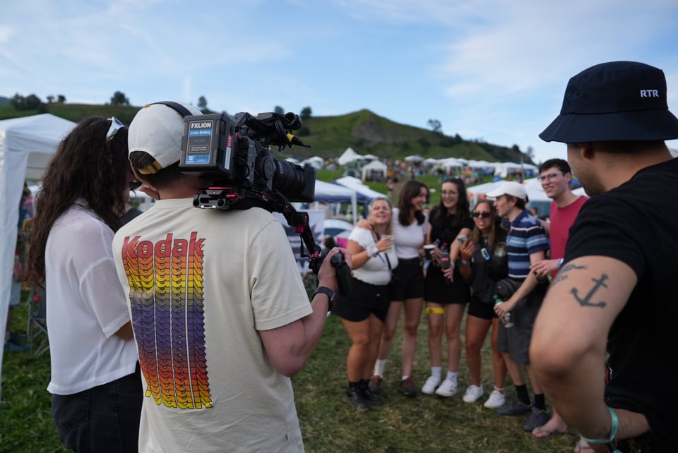 Gruppe von Menschen bei einem Outdoor-Festival, Kamera im Vordergrund.