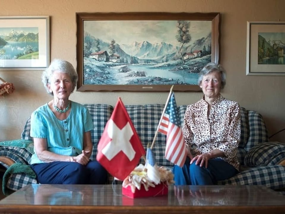 Zwei Frauen sitzen auf einem Sofa, vor ihnen Schweizer und US-Flaggen.