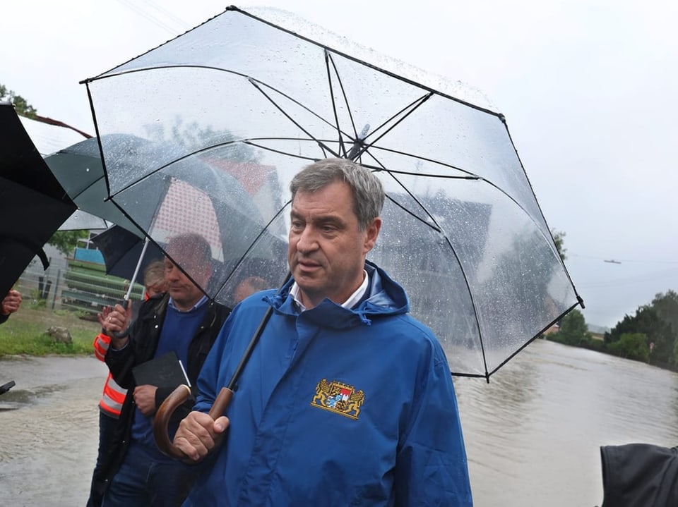 Mann im blauen Regenmantel mit Regenschirm bei Hochwasser.
