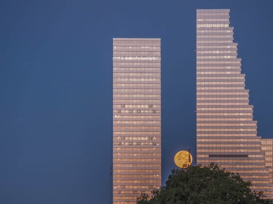 Zwei Hochhäuser mit untergehendem Mond dahinter.